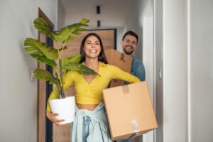 young couple moving out of home carrying plants and boxes in the hall